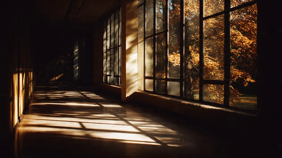 Long institutional corridor with warm golden light falling through high windows, autumn trees visible outside